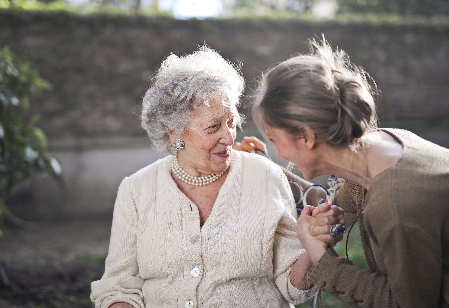 A carer sharing a warm, joyful moment with her elderly client, holding her hands and laughing together outdoors