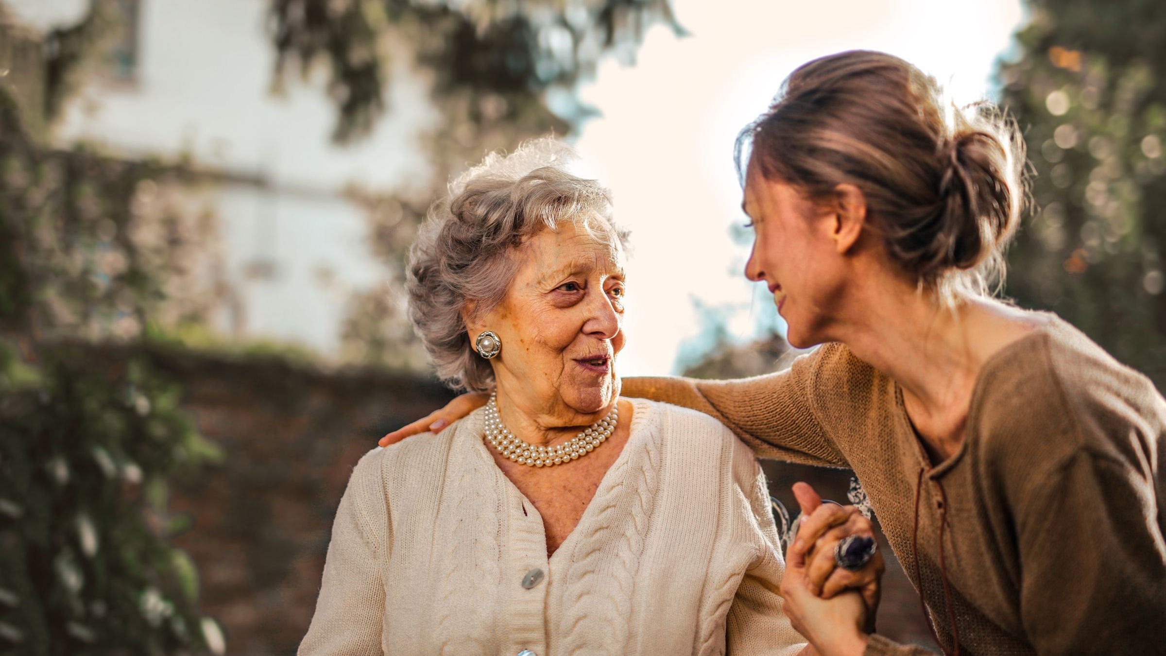 A carer and her client laughing together in a warm, sunlit garden