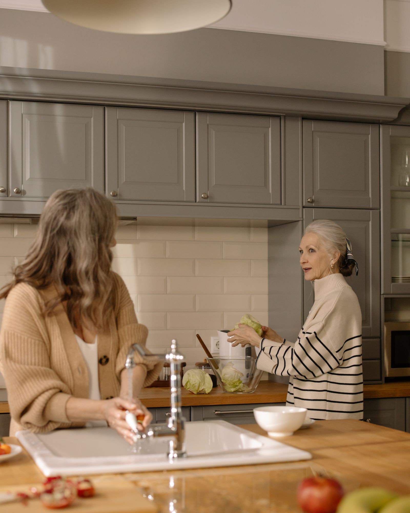 Two women chatting over meal preparation in a bright, elegant home kitchen