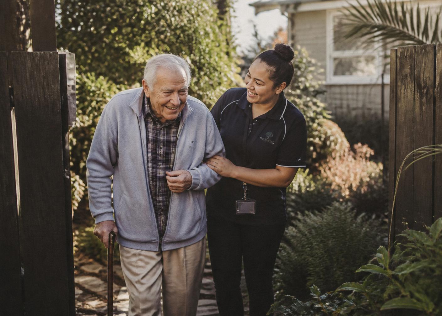 An elderly man walking through the garden with his carer